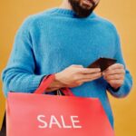 Bearded man holding a sale bag and smartphone in a studio setting.